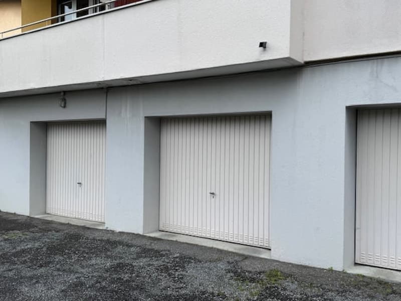 The image shows a multi-story building with several garage doors on the ground floor. The building has a plain, gray exterior with a flat roof.