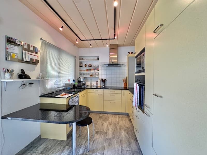 Modern kitchen with yellow cabinets, black countertops, tiled backsplash, open shelving, and a dishwasher