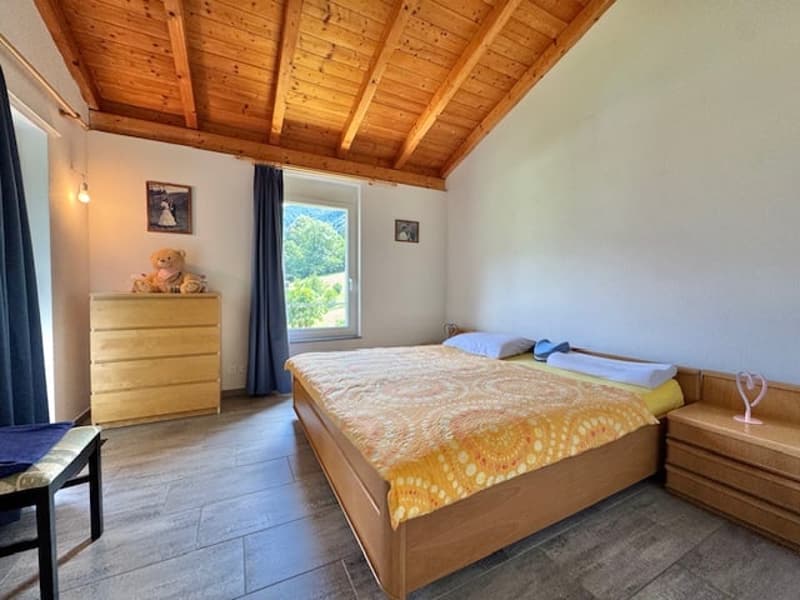 Spacious bedroom with wooden ceiling, large window, wooden dresser, and a double bed with colorful bedding.
