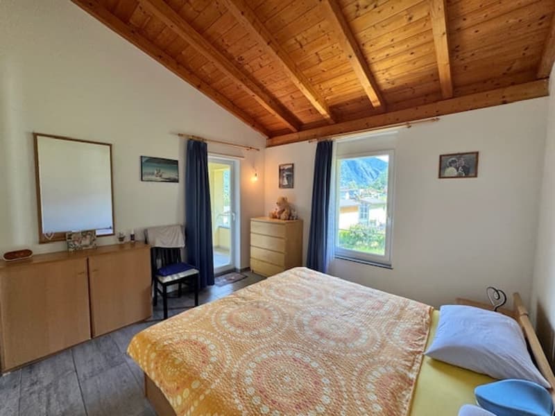 Spacious bedroom with wooden ceiling, large windows, dresser, and a queen-size bed with a colorful quilt.