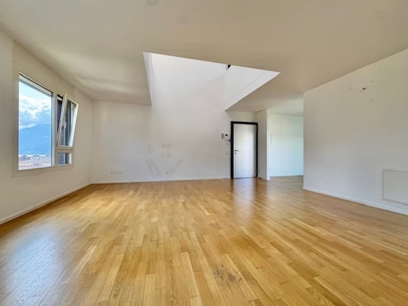 Spacious living room with hardwood flooring, large windows, and a high ceiling with a skylight