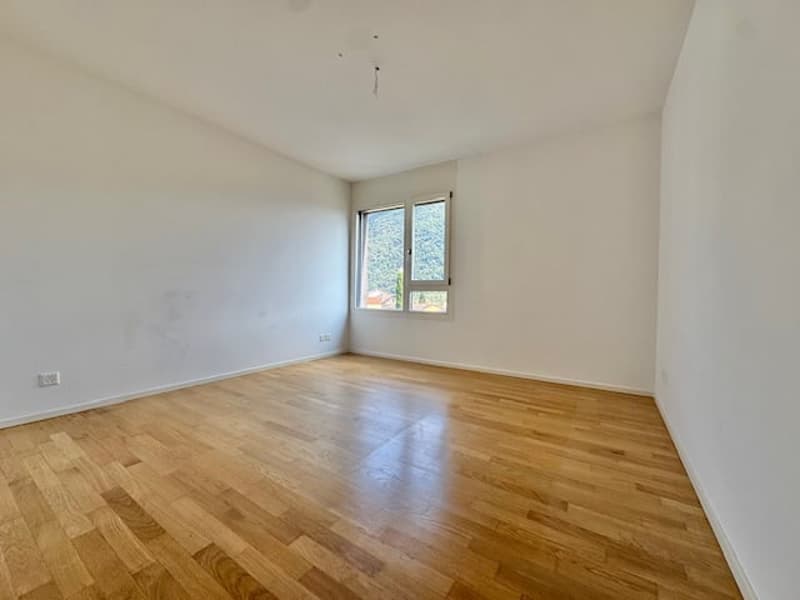 Spacious bedroom with hardwood flooring, white walls, and a large window providing natural light.