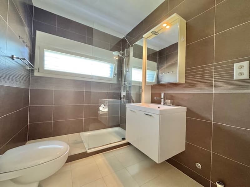 Modern bathroom with brown and white tiles, vanity unit with sink, toilet, and shower enclosure with glass door