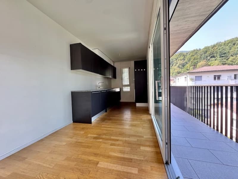Open-plan living area with hardwood floors, modern black kitchen cabinets, and large sliding glass doors leading to a balcony or terrace with a view of the surrounding area.