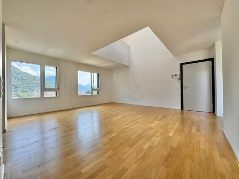 Spacious living room with large windows offering a scenic view, hardwood flooring, and an open, airy layout.