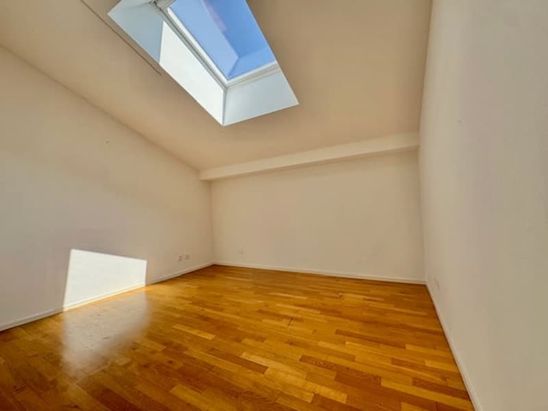 Spacious room with hardwood flooring, white walls, and a skylight providing natural light.