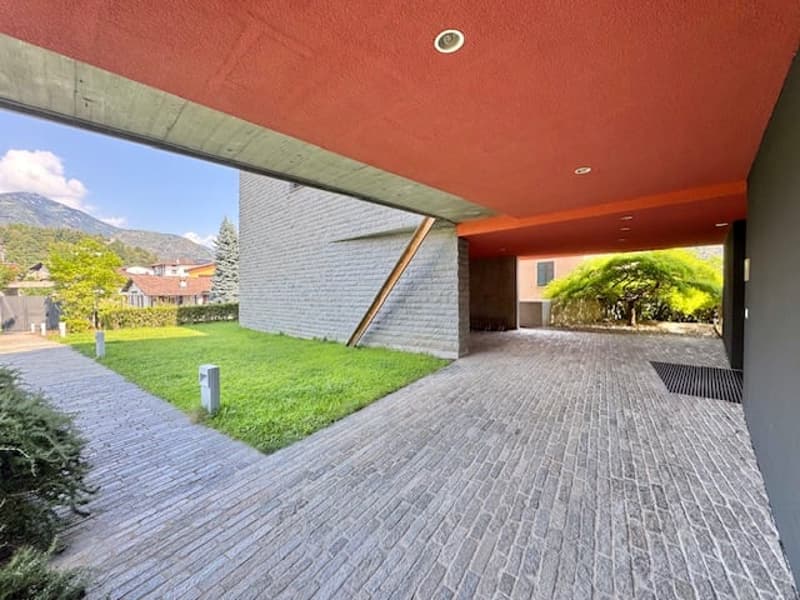 Modern two-story house with a covered patio area, brick exterior, and a grassy lawn. The patio has a concrete floor and leads to the backyard.