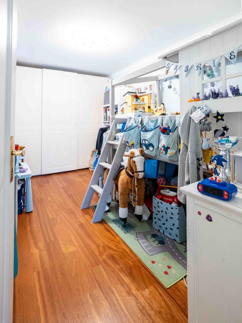 a child's room with a wooden floor, bunk bed, rug, toys, and storage boxes