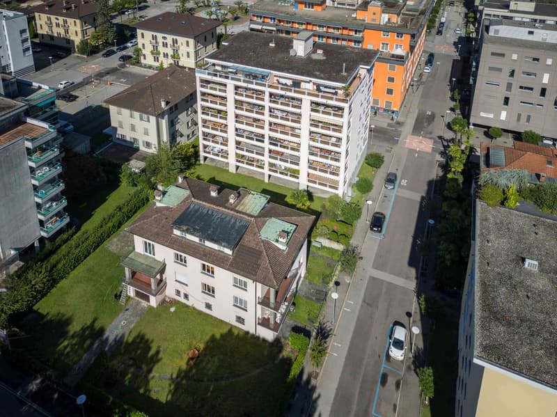 Multiple buildings of various heights, multistory parking lot, green lawn areas, several cars parked