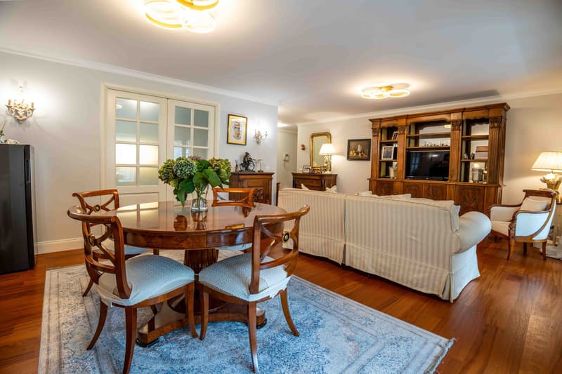 dining room with wooden table and chairs, blue carpet, living room with white sofa, wooden entertainment center, lamps, TV, and wooden floor