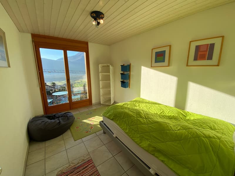 Slim double bed, lime green quilt, green carpet, glass door, shelf with storage baskets, picture frames, wooden ceiling