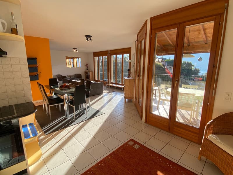 Dining room with white tiles, large windows, glass doors leading to balcony, dining table, kitchen, windows overlooking the mountains