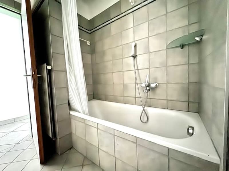 white bathtub, shower with glass curtain, wall-mounted radiator, tile flooring
