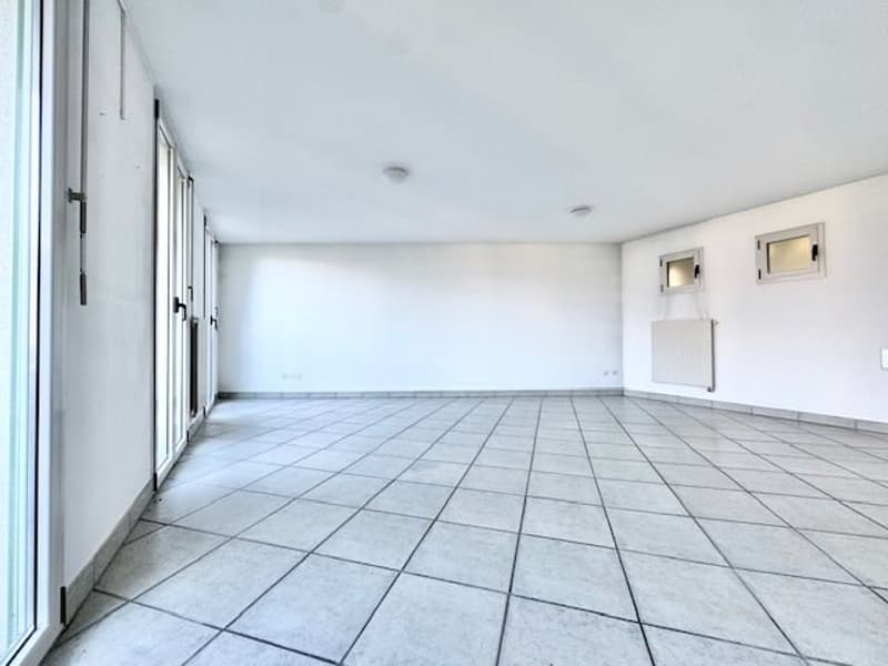 Empty room with tiled floor, white walls, and glass doors. Two small windows on the wall with a heating unit below one.