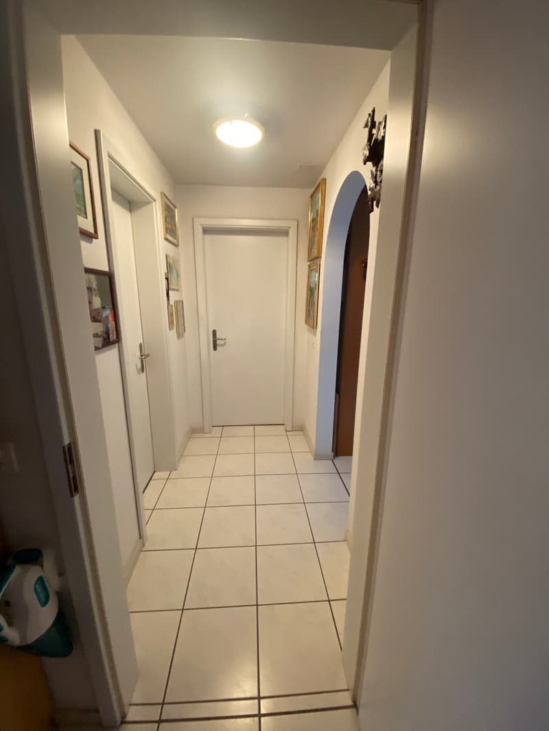 tiled corridor, white walls, framed pictures on the wall, a door at the end of the corridor