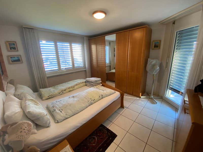 Bedroom with two beds, wooden wardrobe, tiled floor, window with blinds, ceiling light, rug, decorative pillow