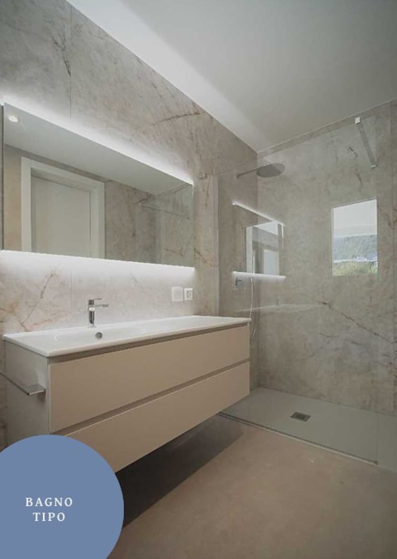 Bathroom with marble walls, a vanity with a sink, and a glass shower enclosure.