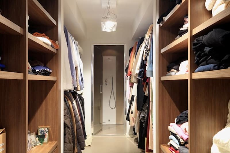 Dressing room with multiple wooden shelves filled with clothes and accessories, a central hallway, and a glass door.