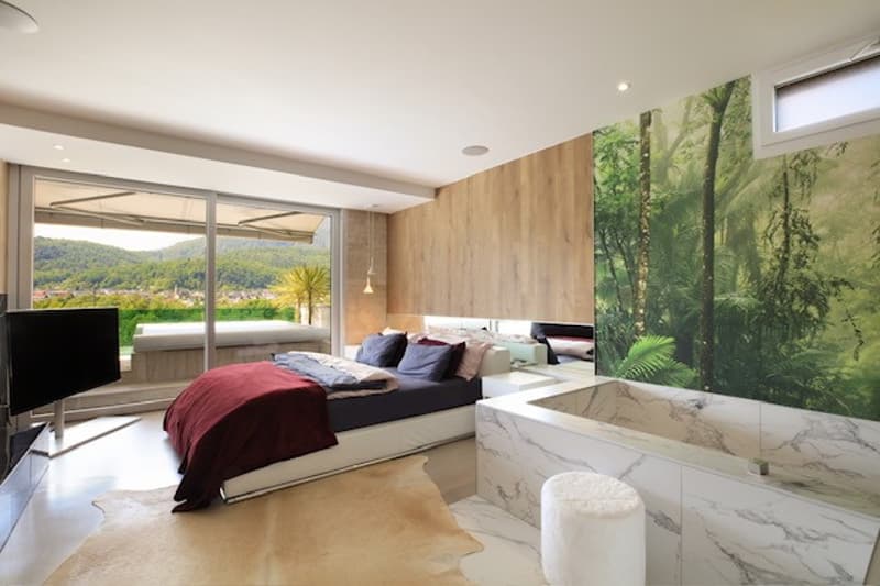 Large bed, wooden wall, white ceiling, flat screen television, wooden floor, large bathtub, white rug