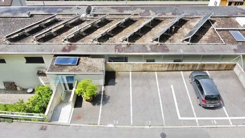 solar panels on roof, gray car parked, 4 parking spaces, potted plant at entrance