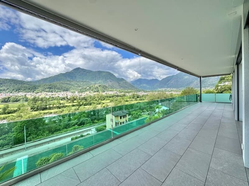 Large balcony with glass railing, overlooking a scenic landscape with mountains and lush greenery in the distance