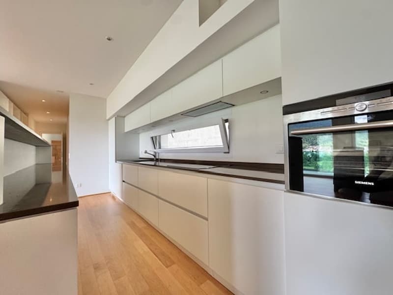 Modern, minimalist kitchen with white cabinets, wooden countertops, and stainless steel appliances including a dishwasher.