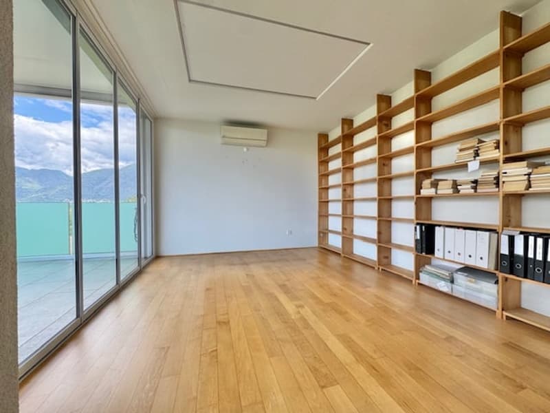 Large open room with hardwood floors, floor-to-ceiling windows providing a scenic view, and built-in wooden shelving units along the walls.