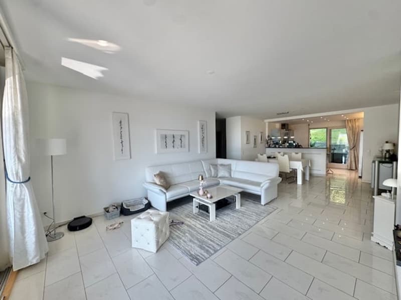 modern living room with white leather sofa, white coffee table, white tile flooring, white walls, white curtains, white floor lamp, white ottoman, white rug, white kitchen with dining table and chairs, white cabinets, white countertops, white appliances