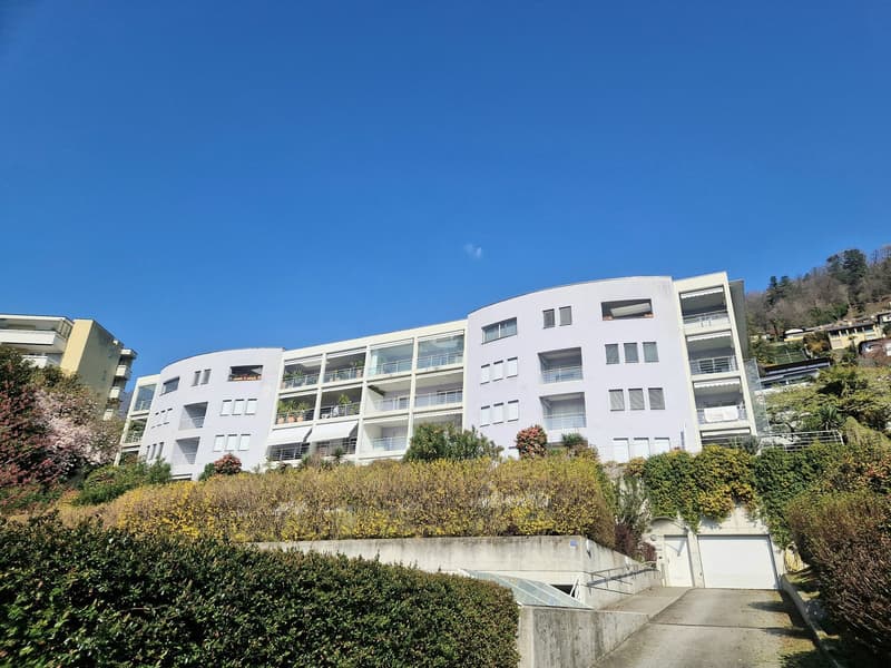 White apartment building, multiple balconies, raised ground floor, garage