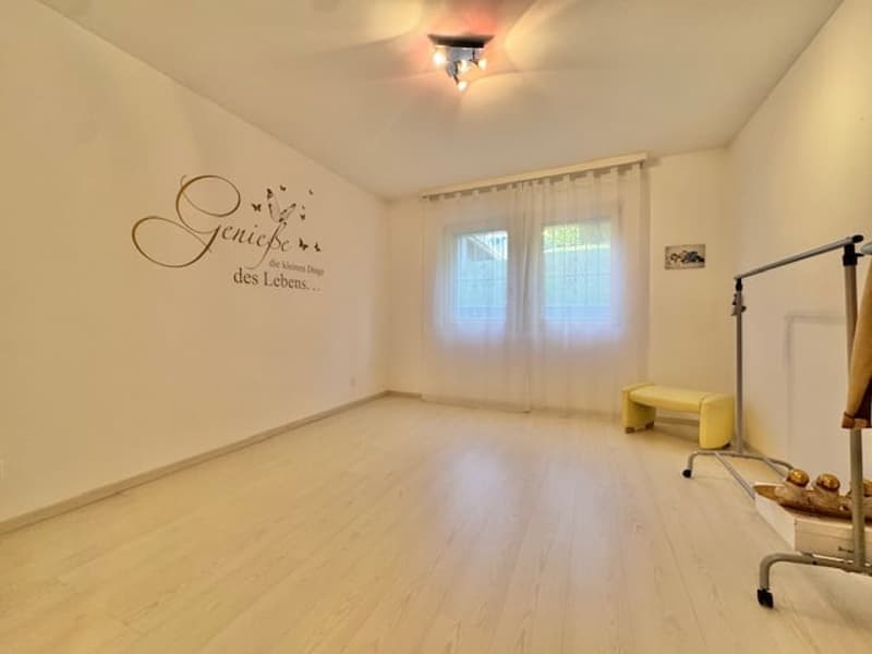 Empty room with white walls, wooden floor, white curtains, yellow bench, wall art, and a metal stand with a rack