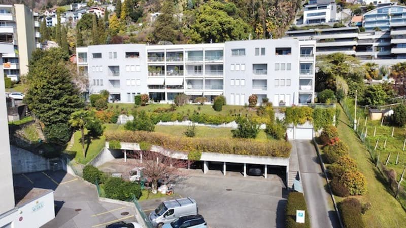A white apartment building with a green roof, underground parking, and a garden in front