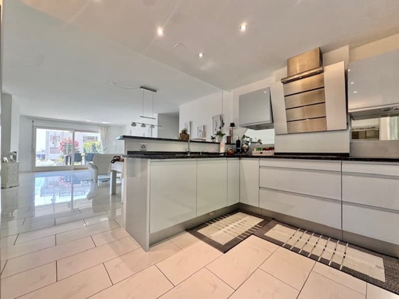 modern kitchen with white cabinets, black countertops, stainless steel appliances, white tiled floor, and a glass door leading to a patio
