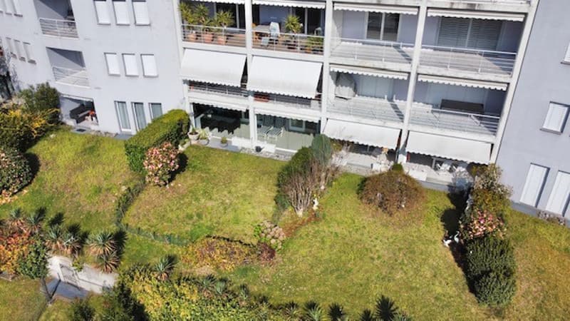 Aerial view of a multi-story building with balconies, a garden in front, and a well-maintained lawn.