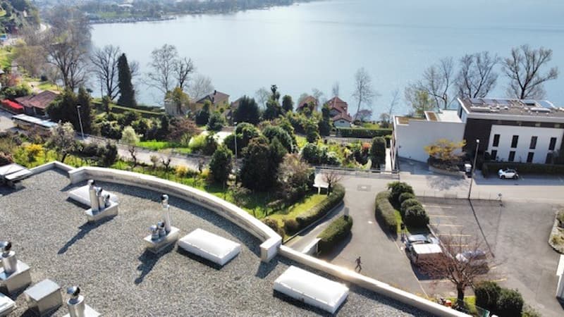 Aerial view of a building with a lake in the background, a parking lot, and a road