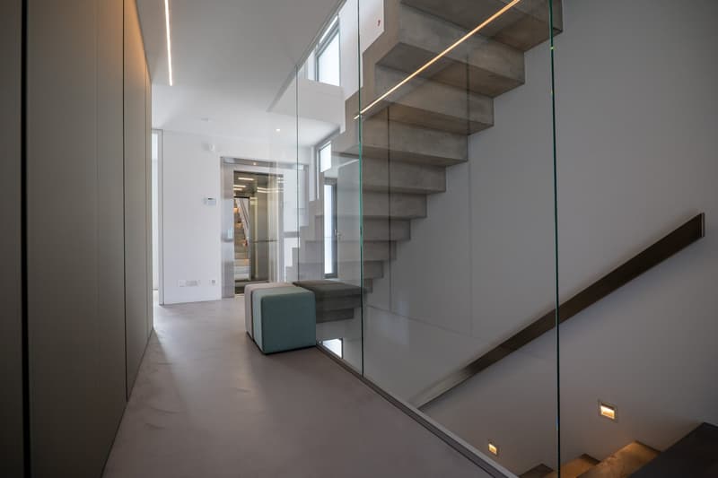modern interior, glass wall, concrete stairs, gray floor, white walls, two ottomans