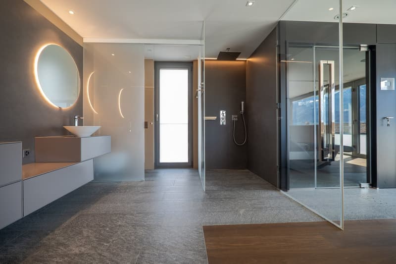 modern bathroom with glass walls, large mirror, white sink, shower with glass door, gray tiles