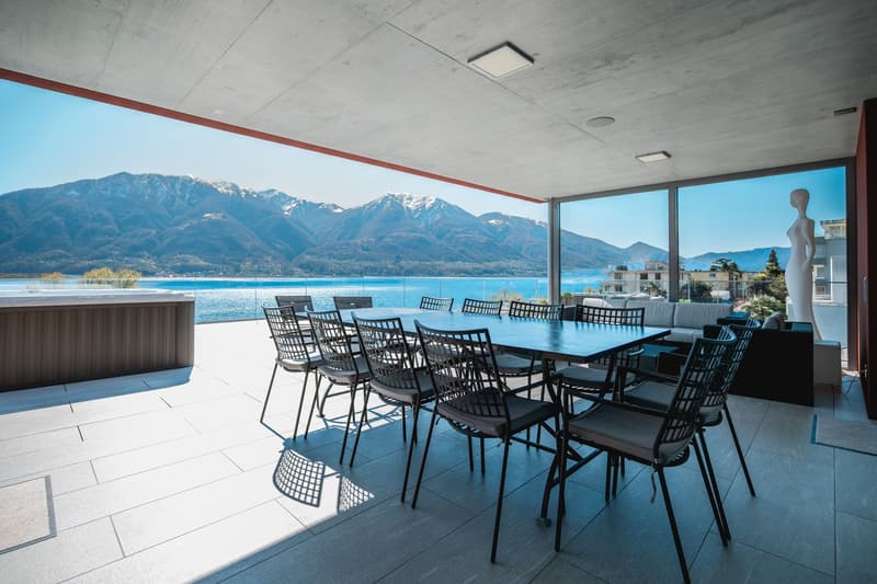 Outdoor dining area with a large table, chairs, and a view of the lake and mountains