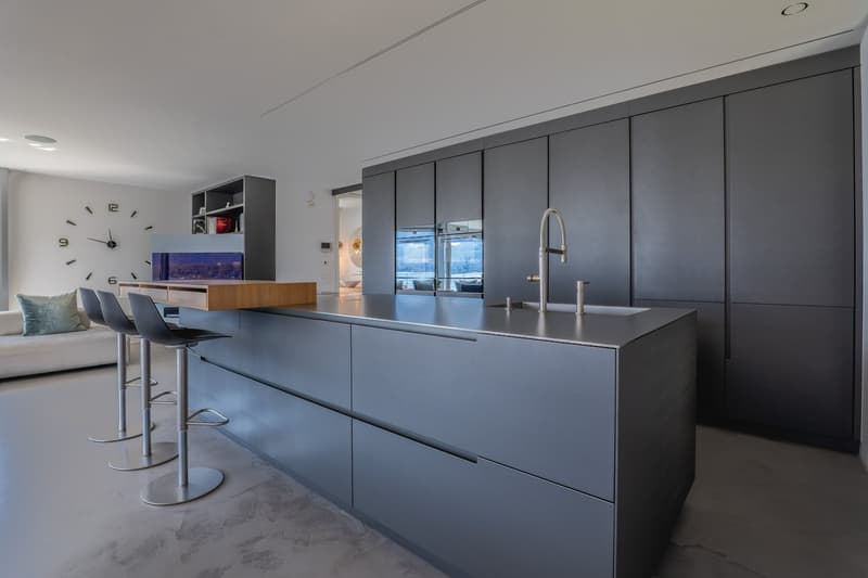 modern kitchen with island, stainless steel countertops, gray cabinets, two stools, large clock on wall