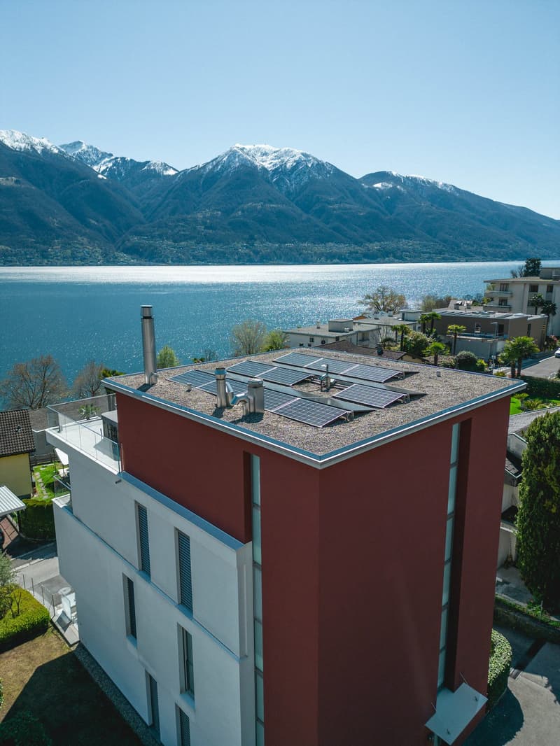 Red and white building with solar panels on the roof, overlooking a lake and mountains