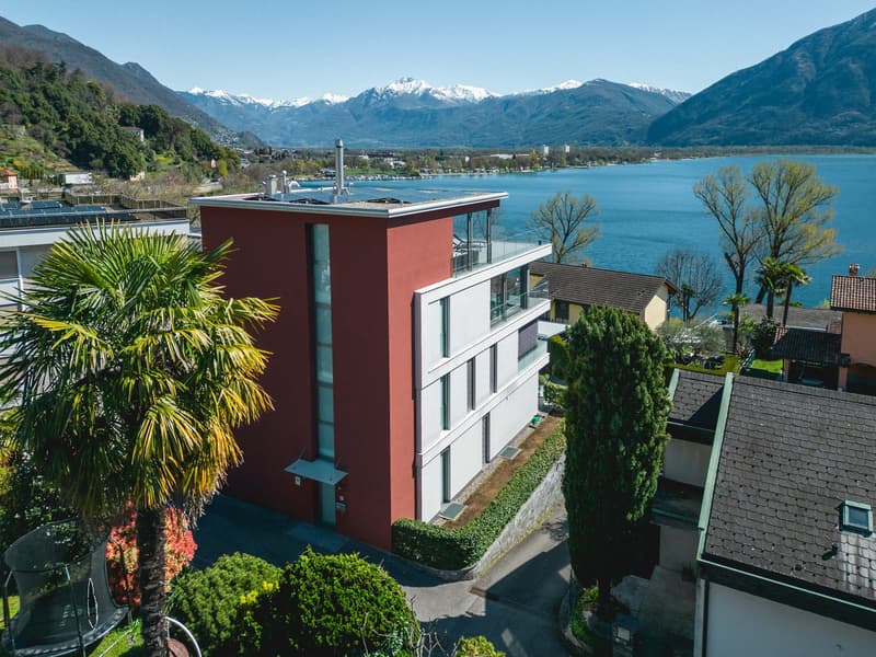 Modern apartment building with red and white facade, solar panels on the roof, balcony, lake view, mountains in the background