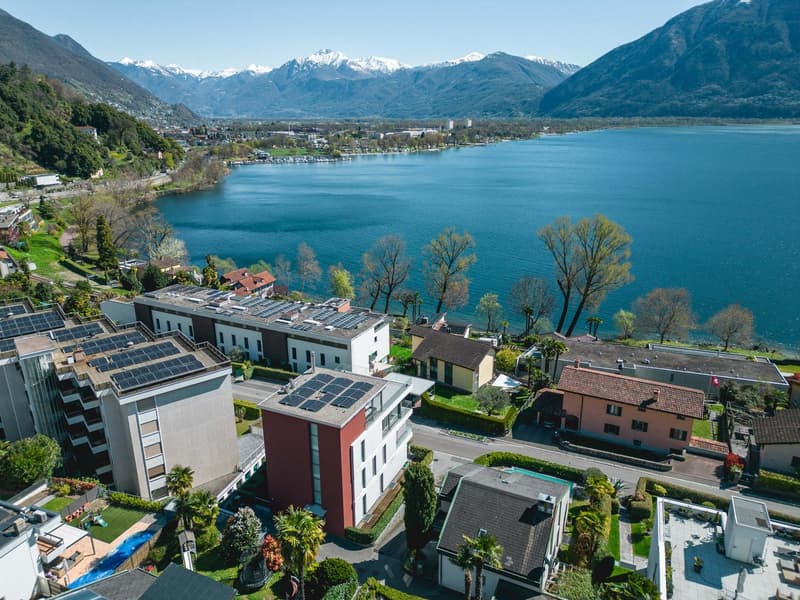 Aerial view of a residential area with buildings, solar panels, a lake, and mountains in the background