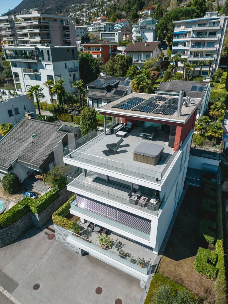 Modern house with solar panels, swimming pool, terrace with hot tub, multiple balconies, large windows, surrounded by greenery
