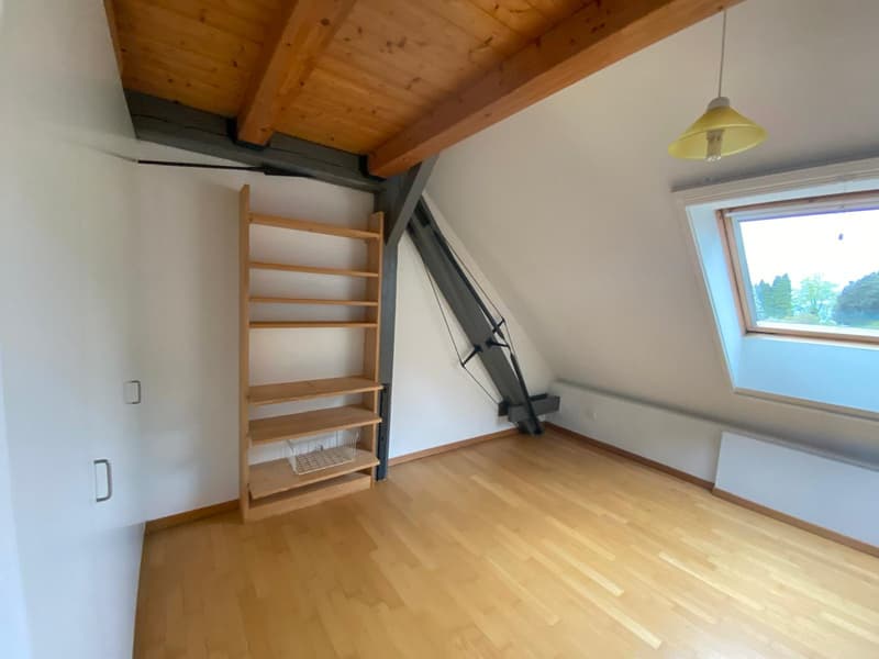 Spacious bedroom with wooden ceiling, hardwood flooring, and a wooden shelving unit. The room has a large window providing natural light and a view of the surrounding landscape.
