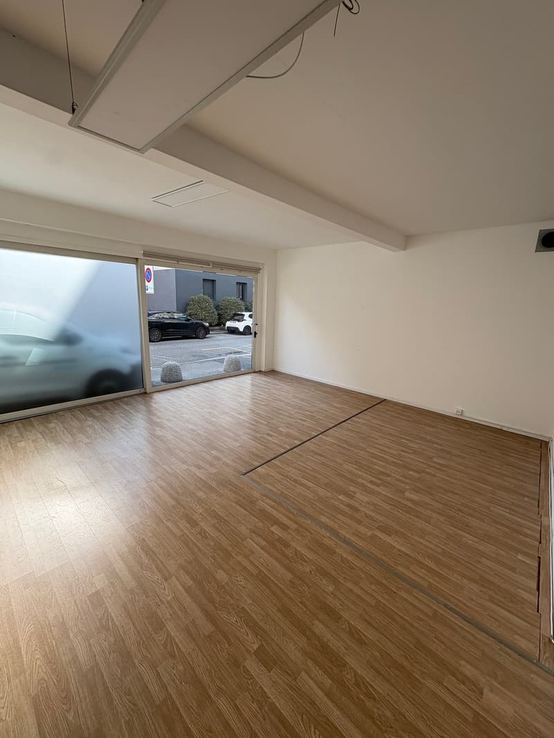 Empty room with hardwood floors, large windows, and glass sliding doors leading to an outdoor parking area.