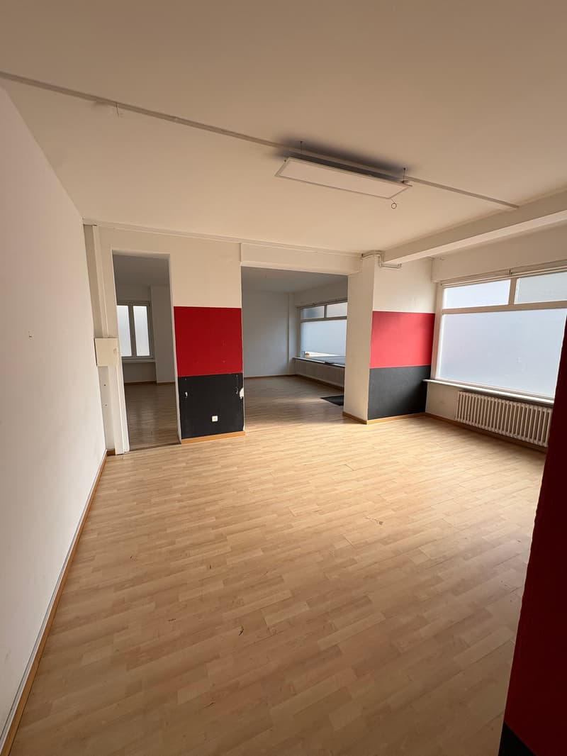 large empty room, wooden floor, large windows, red and black walls