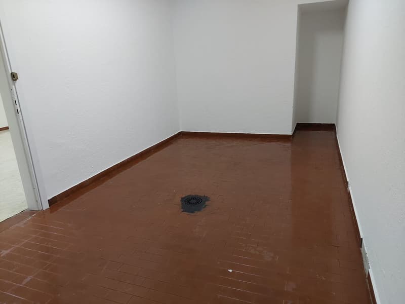 empty room, white walls, brown tiled floor, drain in the center
