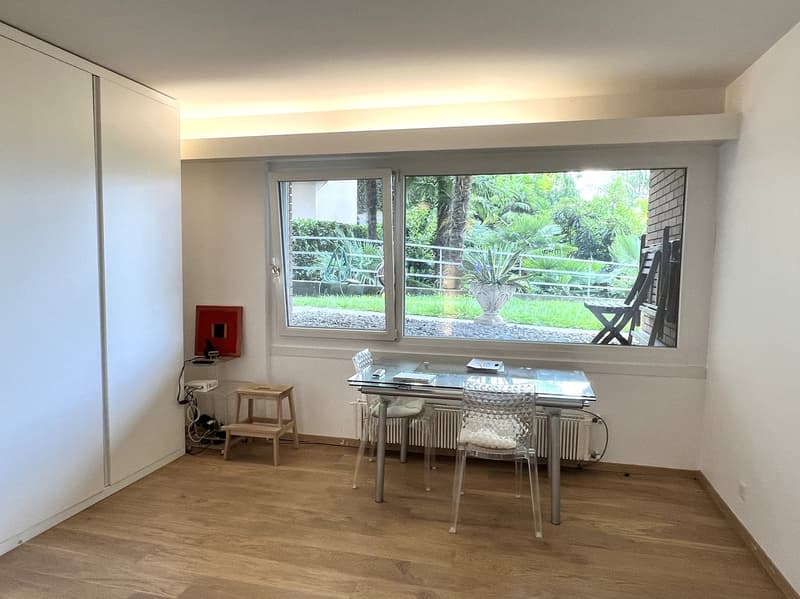 room with desk and chairs, sliding glass door, wooden floor, white walls, window with view of garden