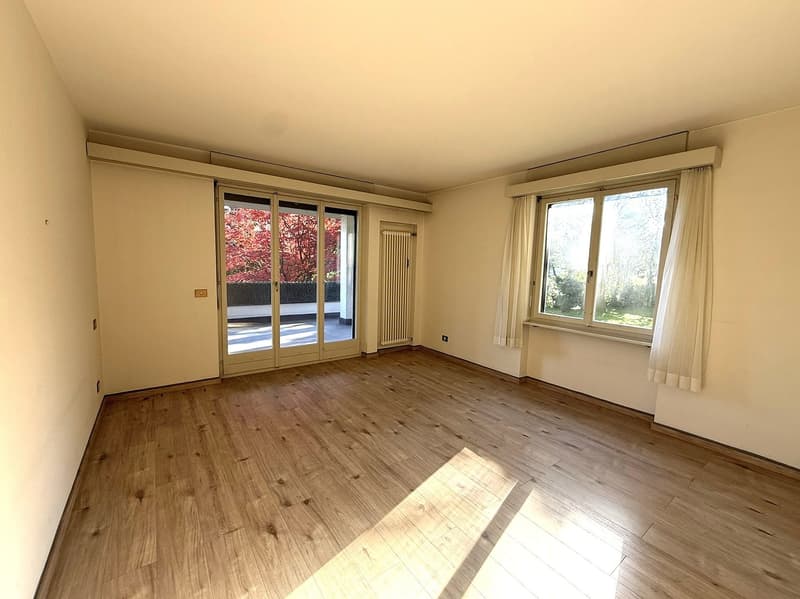 empty room, hardwood floor, large windows, sliding doors leading to balcony, radiator, bright light