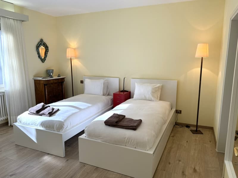 twin bed room, yellow wall, wooden floor, nightstand, lamp, curtains, radiator