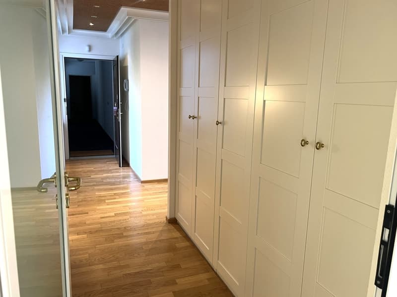 Empty hallway with wooden floors and white walls, built-in wardrobes, open door to another room